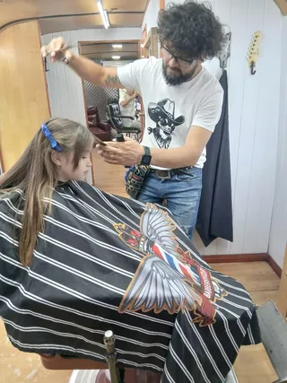 El barbero peina con tijera y peine el pelo largo de una nena sentada en el sillón