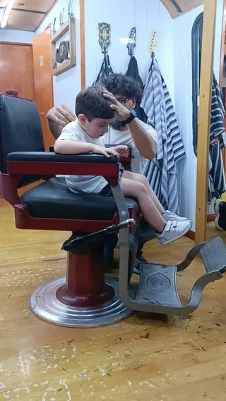 Un nene sentado en el sillón antiguo de barbero mientras le cortan el pelo